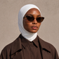Micro Hijab in Weiß, Nahaufnahme mit Schildpatt-Sonnenbrille und braunem Trenchcoat. KI-generiertes Bild.
