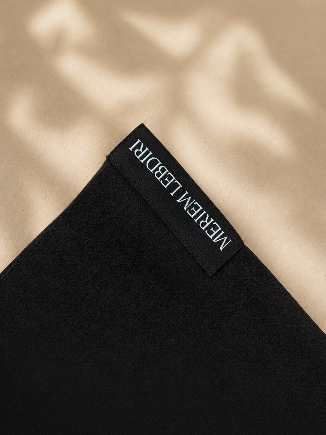 Schwarzer Micro Hijab auf dem Boden, Logo Meriem Lebdiri klar ersichtlich. 