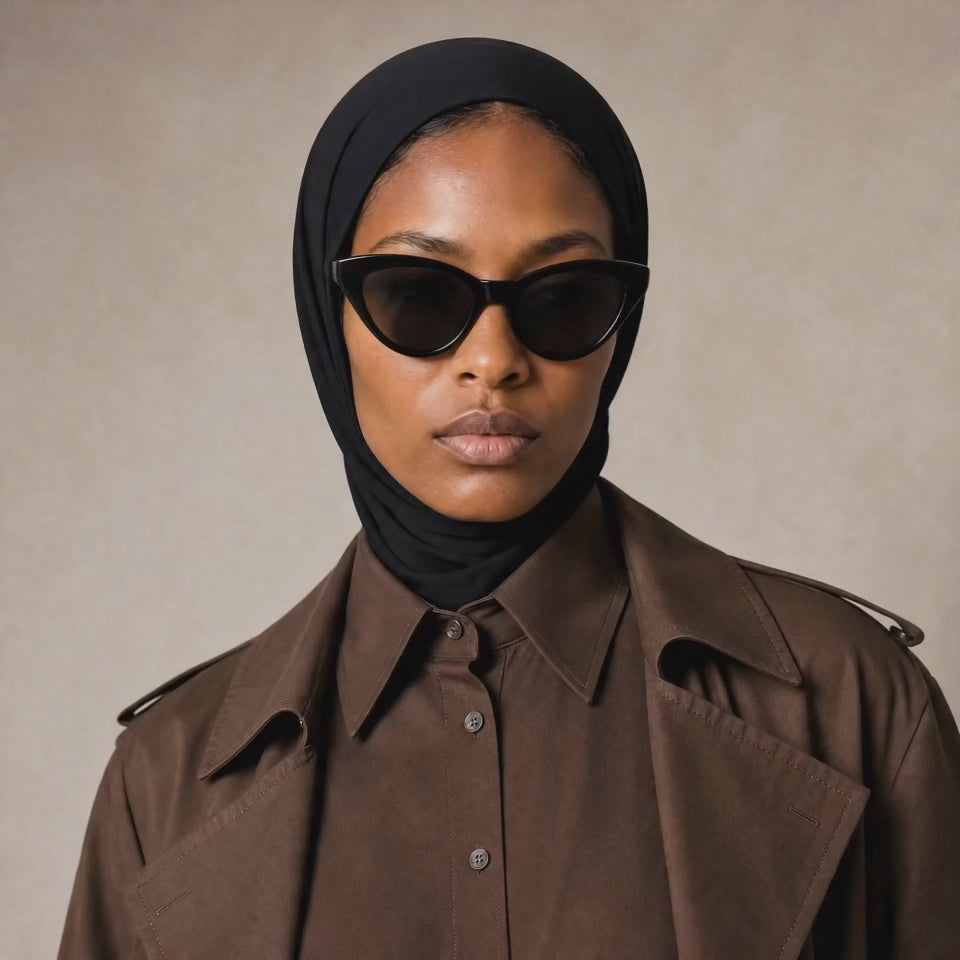 Micro Hijab in schwarz, Nahaufnahme mit Schildpatt-Sonnenbrille, seitlicher Blick, brauner Trenchcoat. KI-generiertes Video.